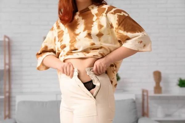 Image of woman trying to do her trousers up after pregnancy weight gain Northampton