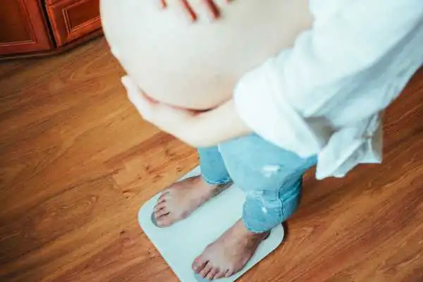 Image of woman weighing herself and experiencing weight gain through pregnancy Northampton